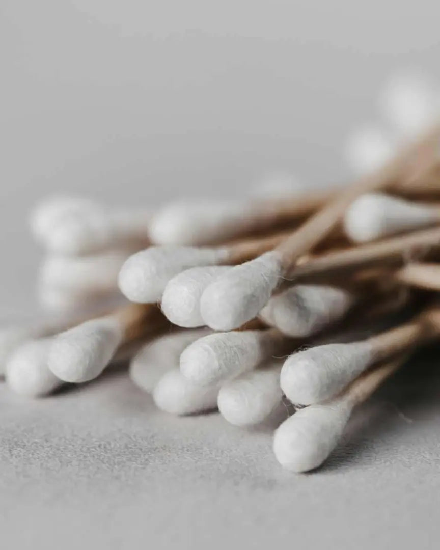 Bastoncillos de algodón orgánico Banbu con palito de madera y puntas de algodón blanco, sobre fondo gris neutro.