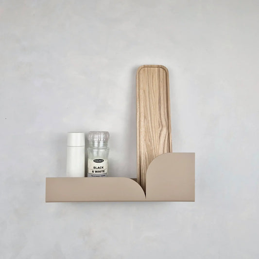 Estante flotante de metal beige con diseño minimalista curvo y una tabla de madera vertical sobre fondo gris claro.