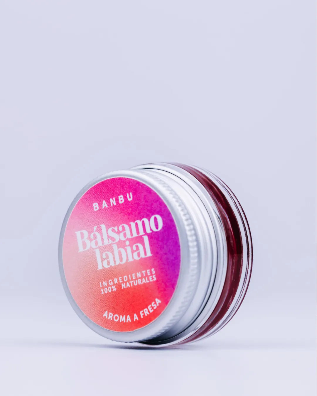 Tarro metálico de bálsamo labial Banbu con etiqueta degradada en rosa y rojo sobre fondo neutro. Producto natural.