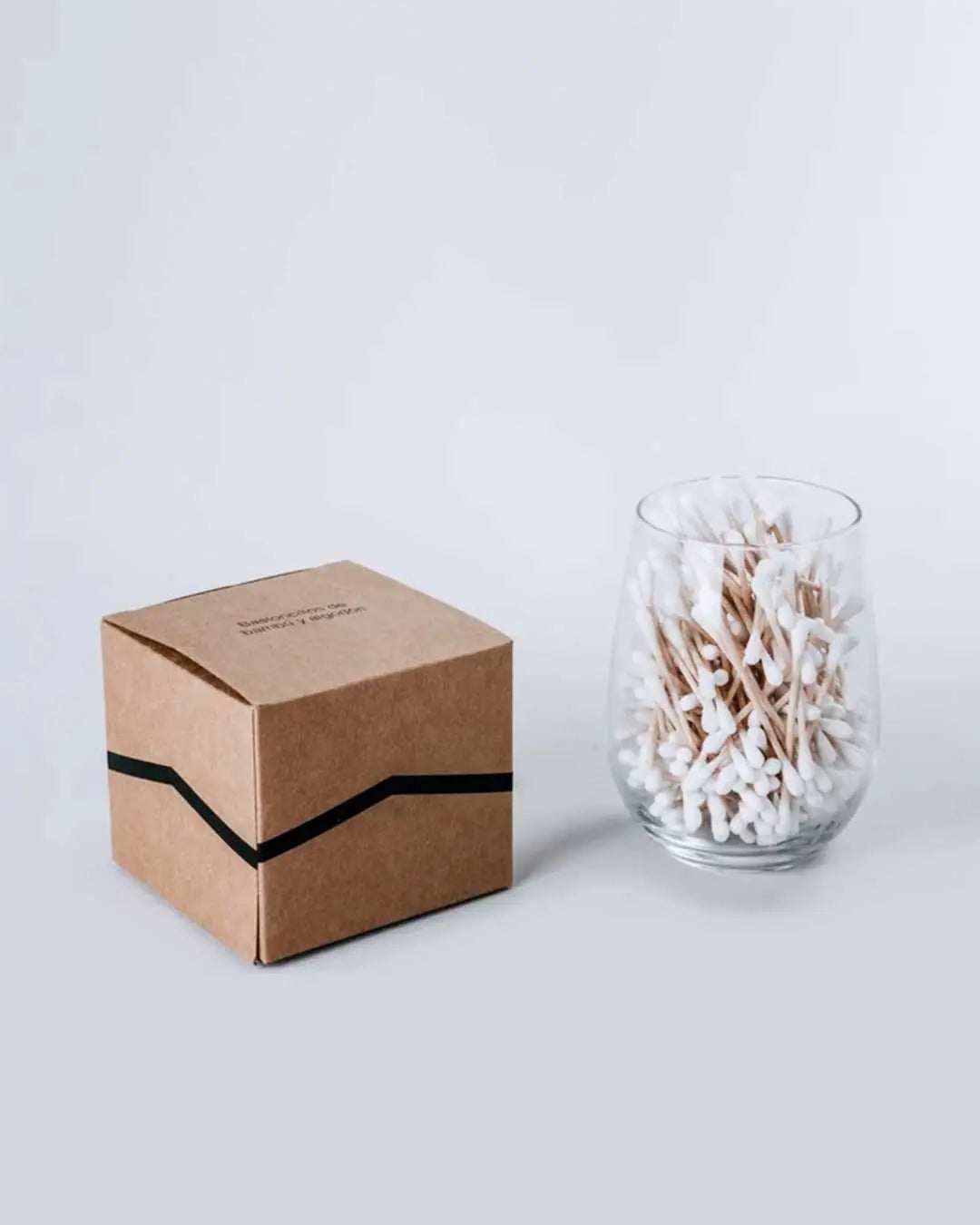 Caja de cartón kraft y vaso con bastoncillos de bambú y algodón orgánico Banbu sobre fondo blanco.