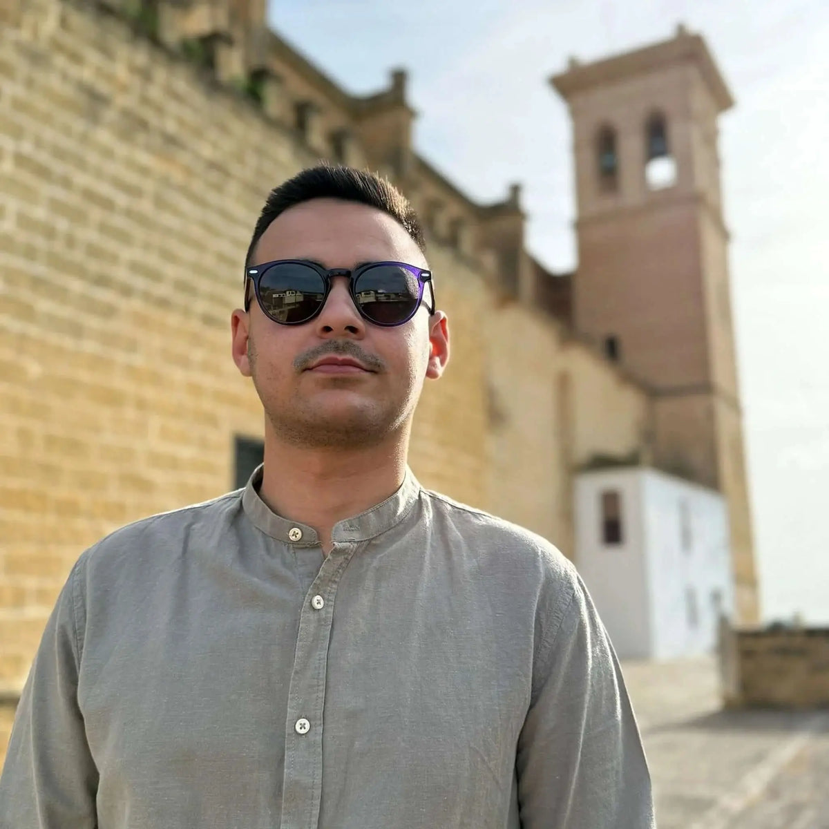 Gafas de sol redondas con montura morada estilo retro, cristales oscuros y detalle metálico, puestas por un hombre.