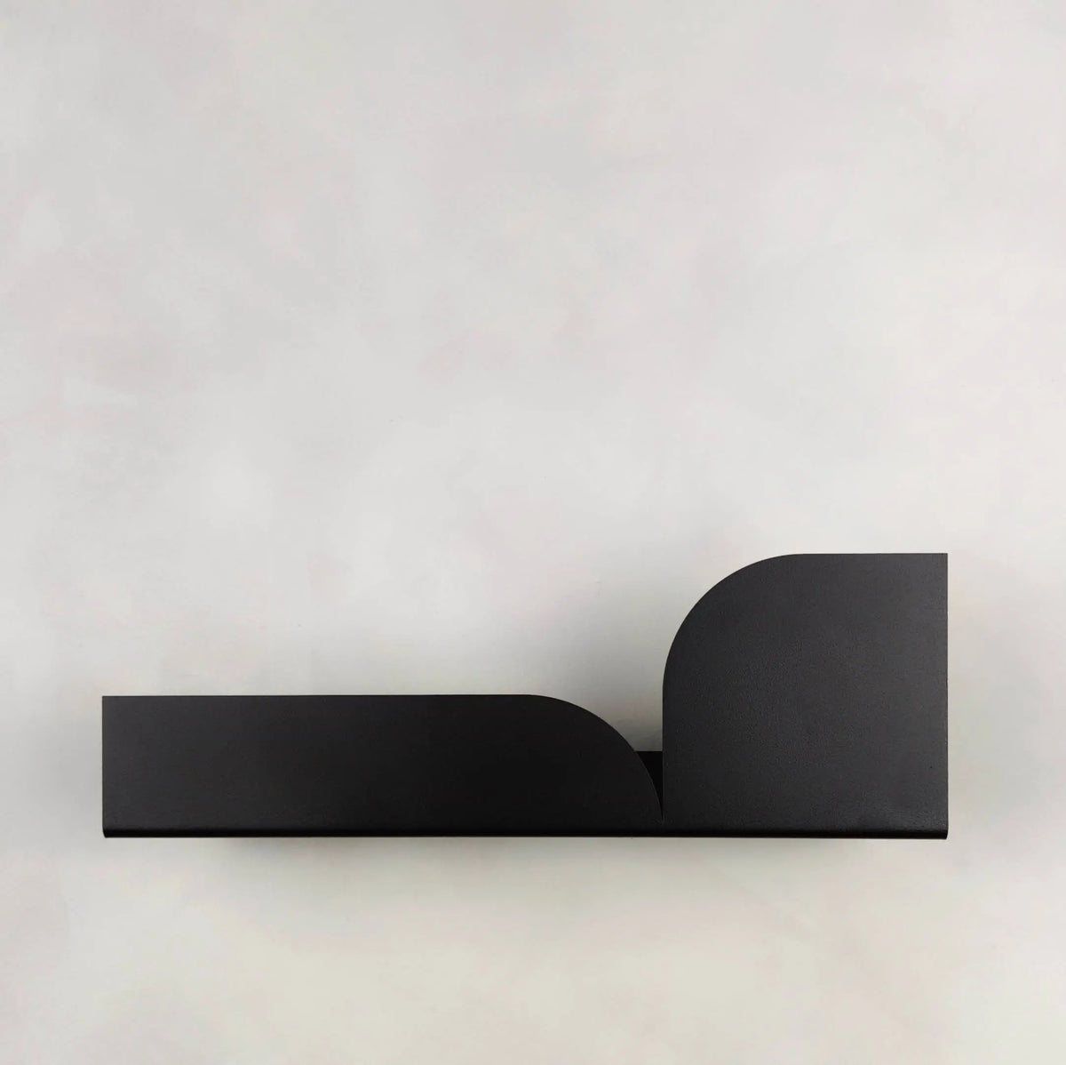 Estante flotante de metal negro con diseño moderno, formas geométricas curvas y acabado mate sobre fondo claro.