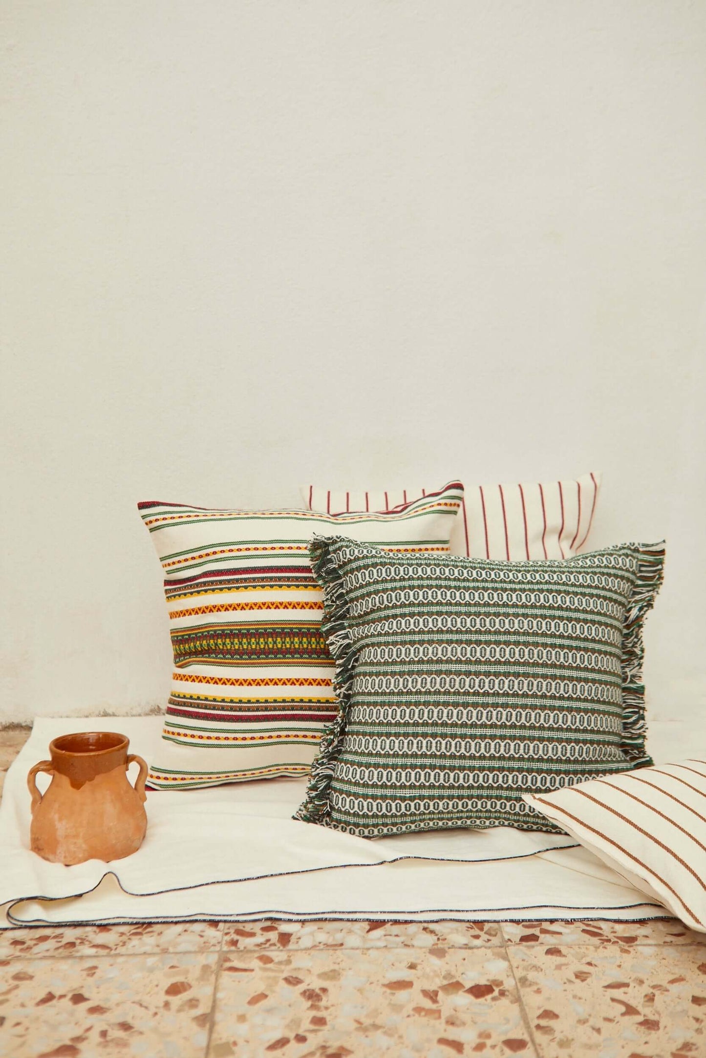 Cojines de loneta con estampados geométricos y rayas, tonos tierra y verde, con detalles de flecos decorativos.