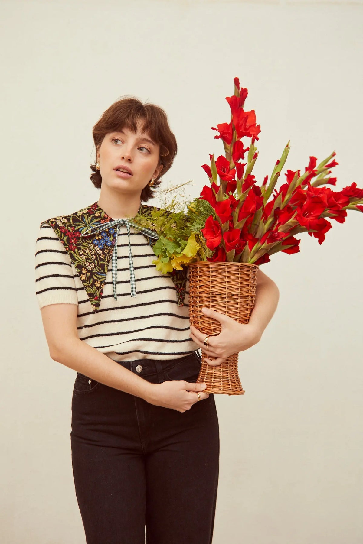 Jarrón pequeño de mimbre natural con diseño trenzado estilo rústico, sostenido por una mujer con flores rojas.