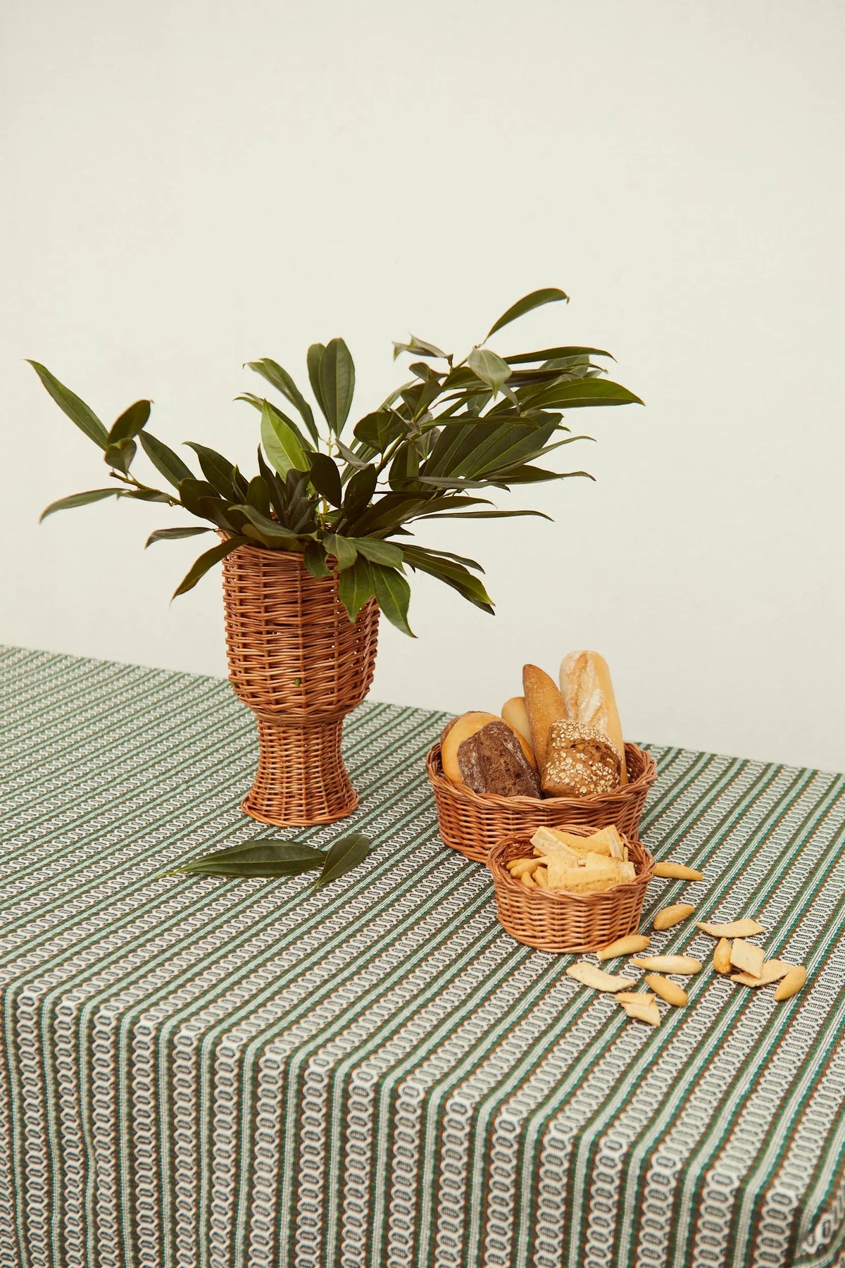 Three natural wicker baskets in different shapes on a green and white striped tablecloth with bread and greenery.