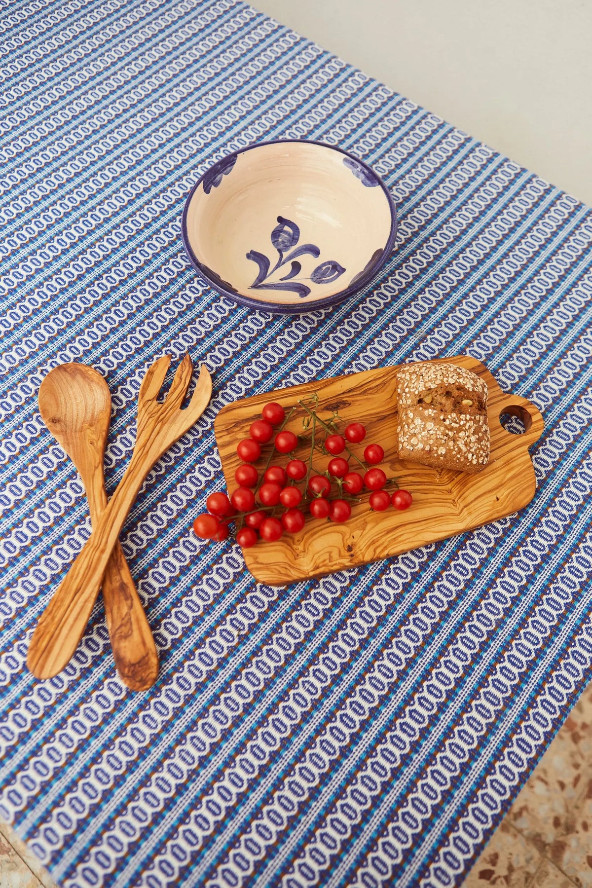 Mantel azul con estampado geométrico tipo ojo de perdiz, sobre el que descansan un bol, cubiertos y una tabla de madera.