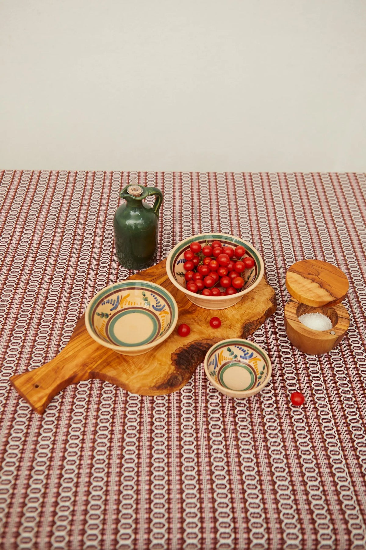 Set of three hand-painted ceramic bowls with colorful geometric patterns, arranged on a rustic olive wood board.