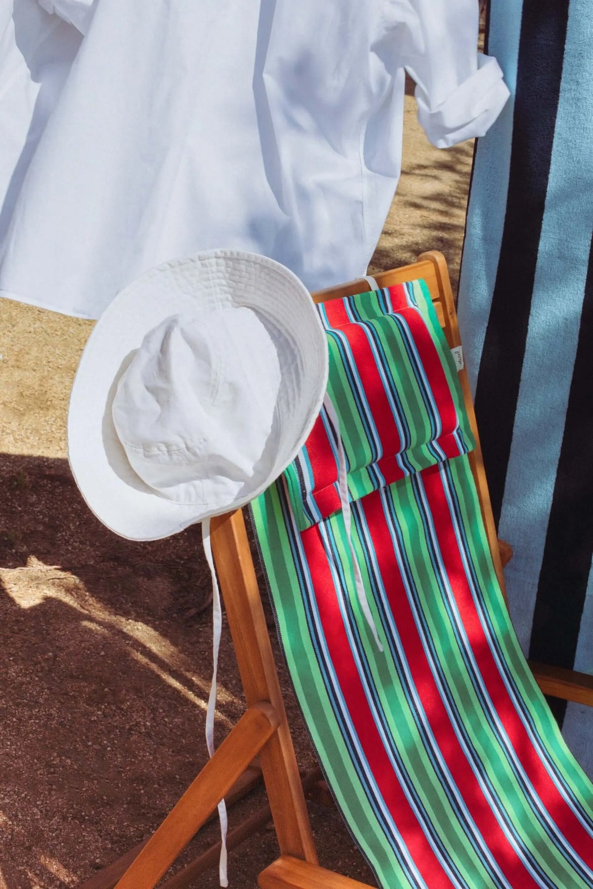 Hamaca de madera con tejido de lona a rayas verticales rojas y verdes, incluye un cojín a juego y un sombrero blanco.