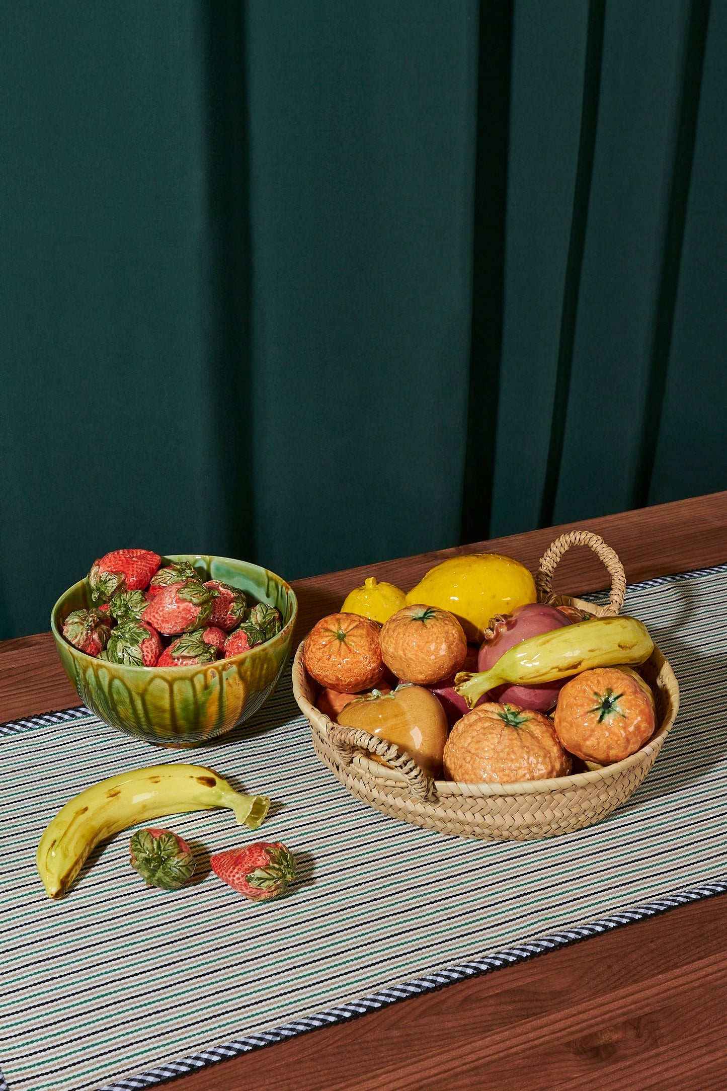 Frutas variadas en cestitas de mimbre y cerámica verde, sobre mesa de madera con mantel a rayas.
