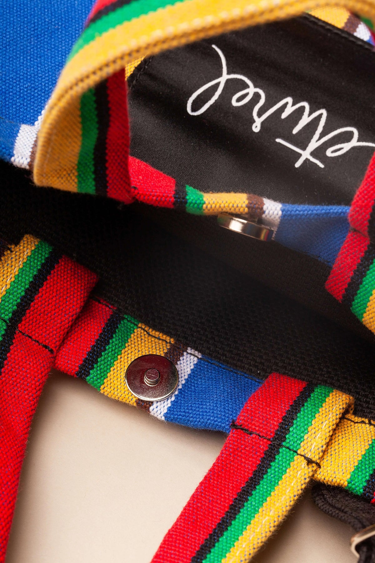 Multi-colored striped canvas crossbody bag with a black interior, magnetic button closure, and matching fabric straps.