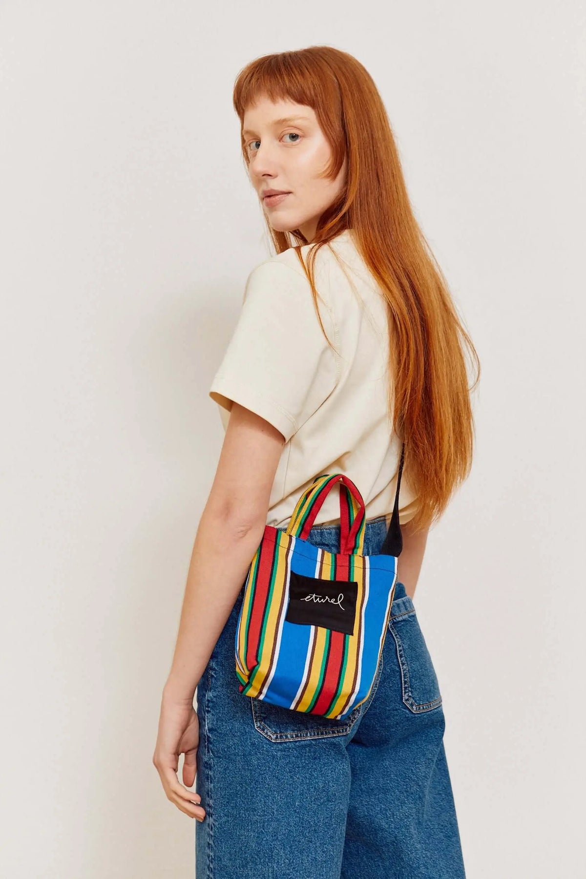 Mini canvas crossbody bag featuring colorful blue, red, yellow, and green stripes with a black brand patch.