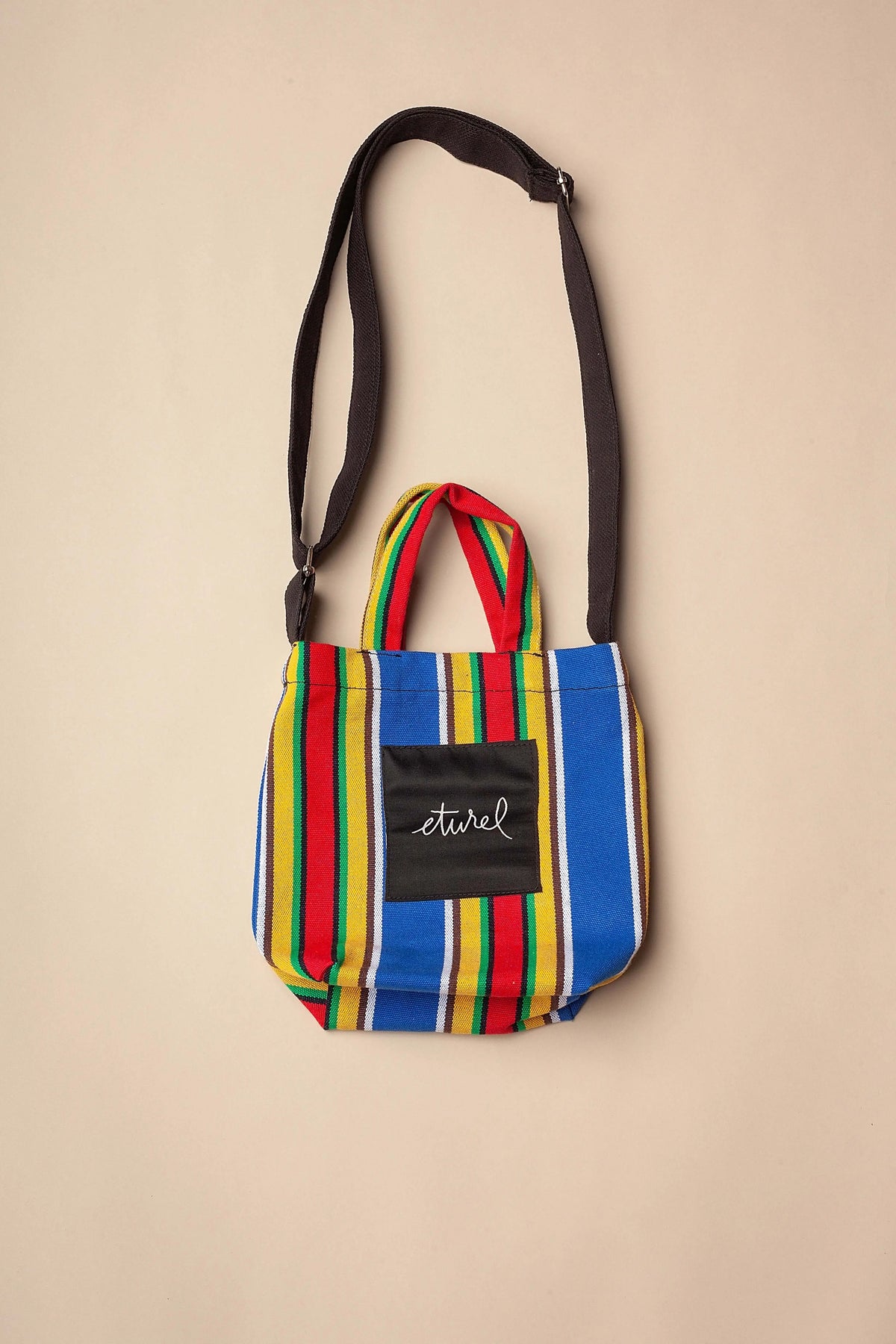 Bolso bandolera mini de lona con rayas verticales multicolor y asas cortas, con correa larga ajustable negra.