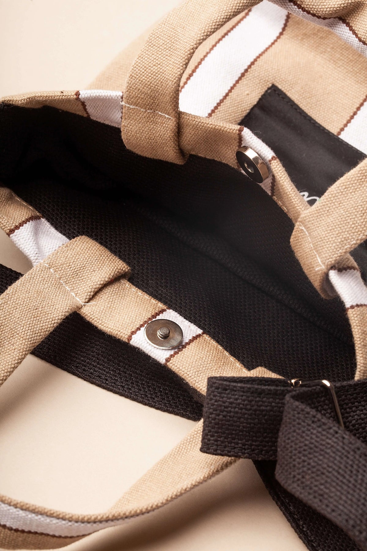 Mini beige and white striped canvas crossbody bag with dark interior, magnetic snap button closure, and shoulder strap.