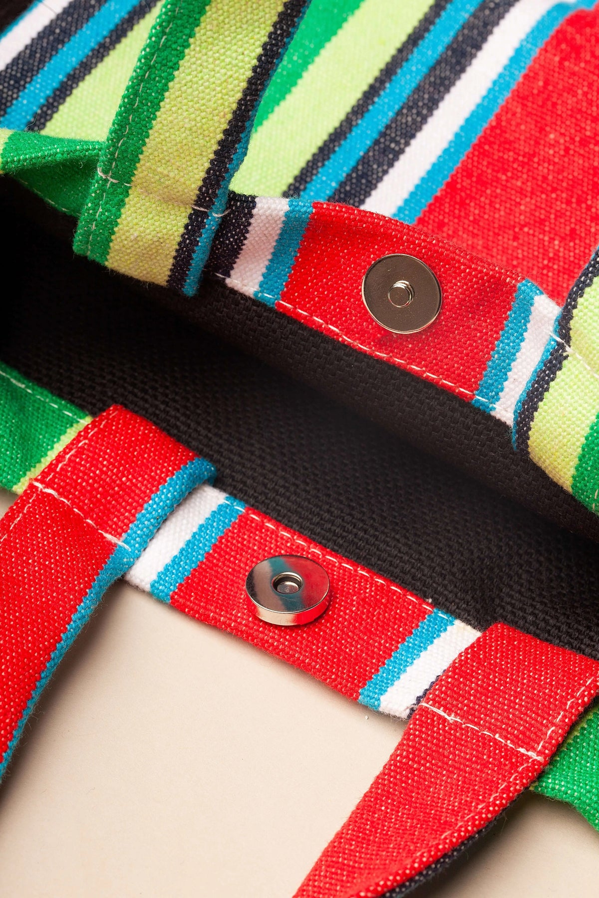 Bolso bandolera de lona a rayas multicolor con cierre de botón magnético y diseño estilo hamaca.