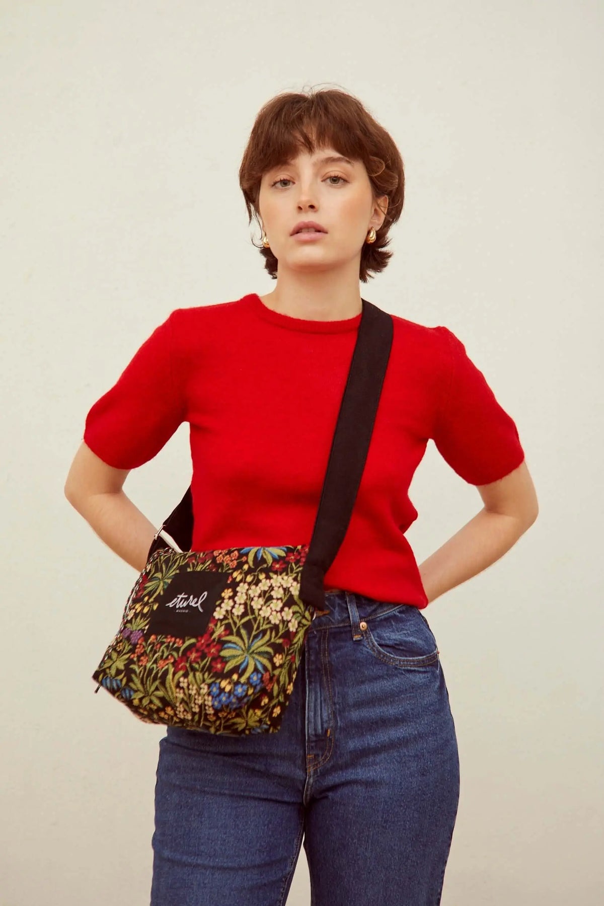 Bolso bandolera de jacquard con estampado de flores coloridas sobre fondo negro y correa ajustable negra.