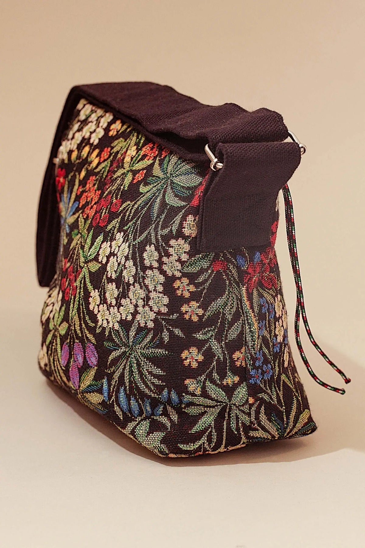 Black jacquard crossbody bag featuring a vibrant, multi-colored floral pattern, black strap, and drawstring closure.