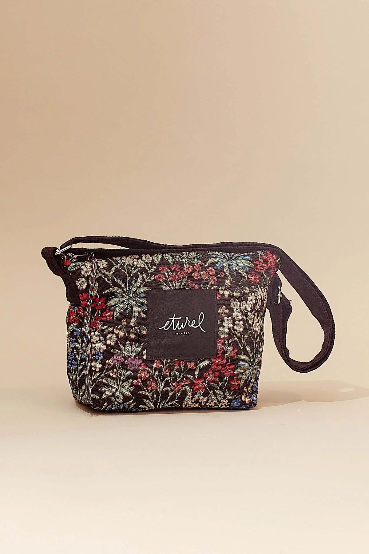 Bolso bandolera de tejido jacquard negro con estampado floral multicolor de margaritas y flores pequeñas.