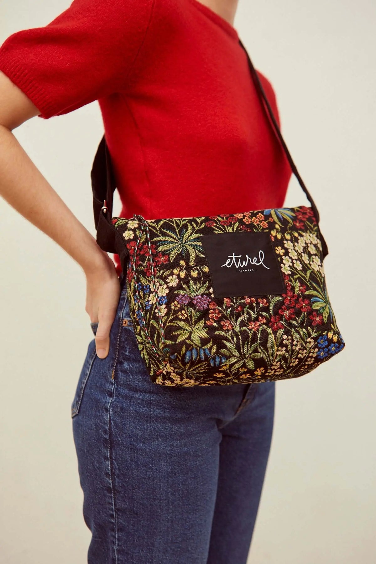Bolso bandolera de jacquard con estampado de flores coloridas sobre fondo negro y correa ajustable.