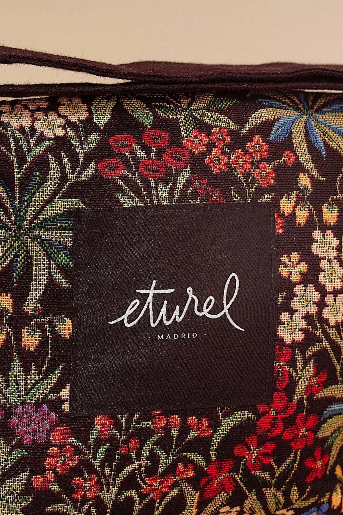 Bolso bandolera de tejido jacquard con estampado floral multicolor de margaritas y flores sobre fondo oscuro.
