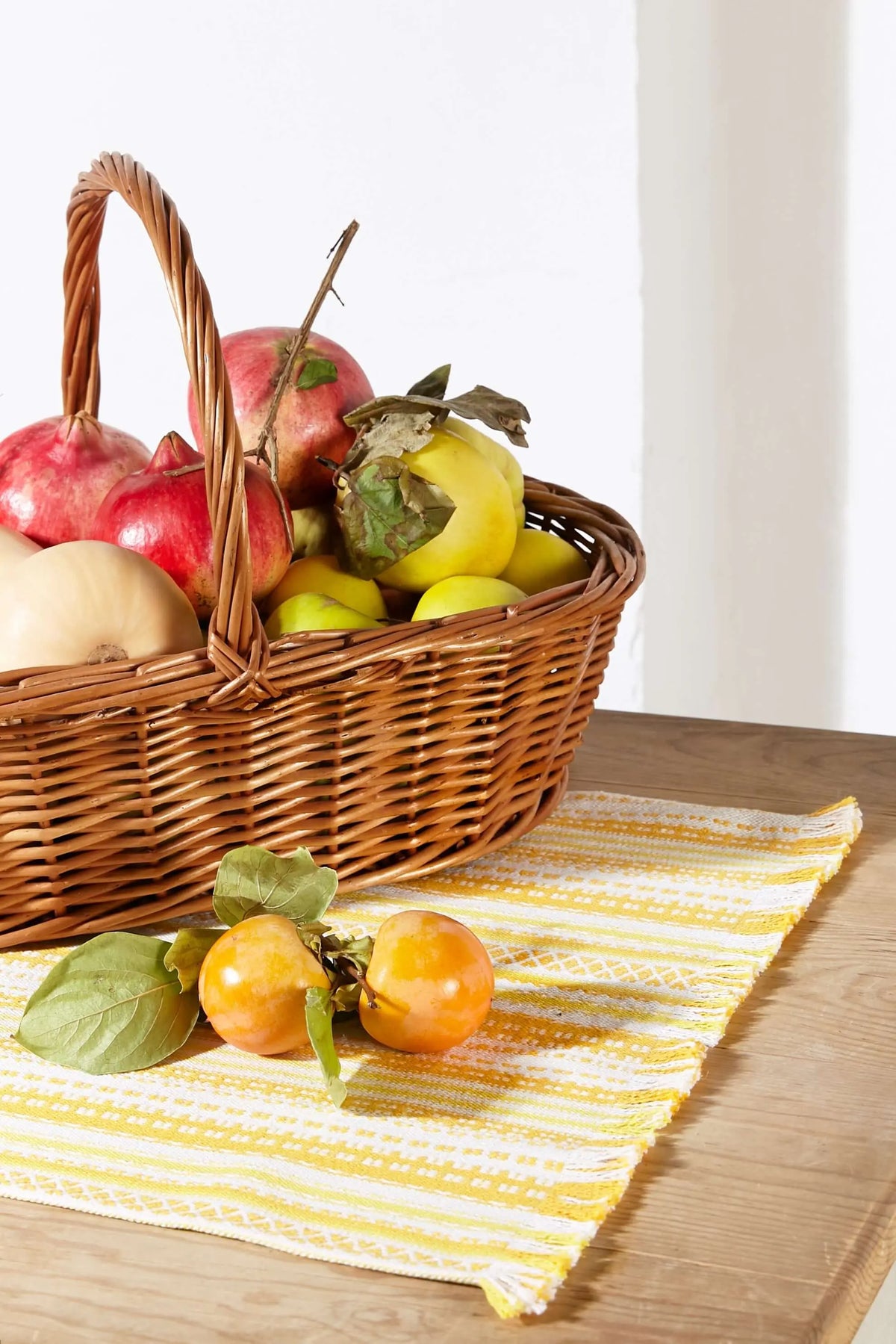 Camino de mesa de tela tejido en tonos amarillos y blancos con textura, sobre mesa de madera con cesta de fruta.
