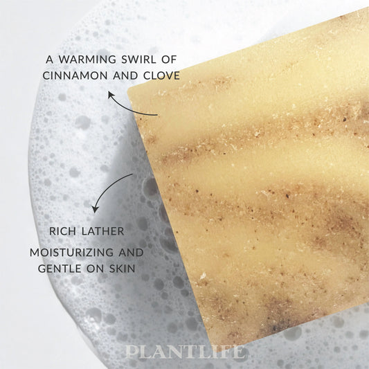 A rectangular bar of tan soap with brown swirls, partially submerged in a rich white lather against a white background.