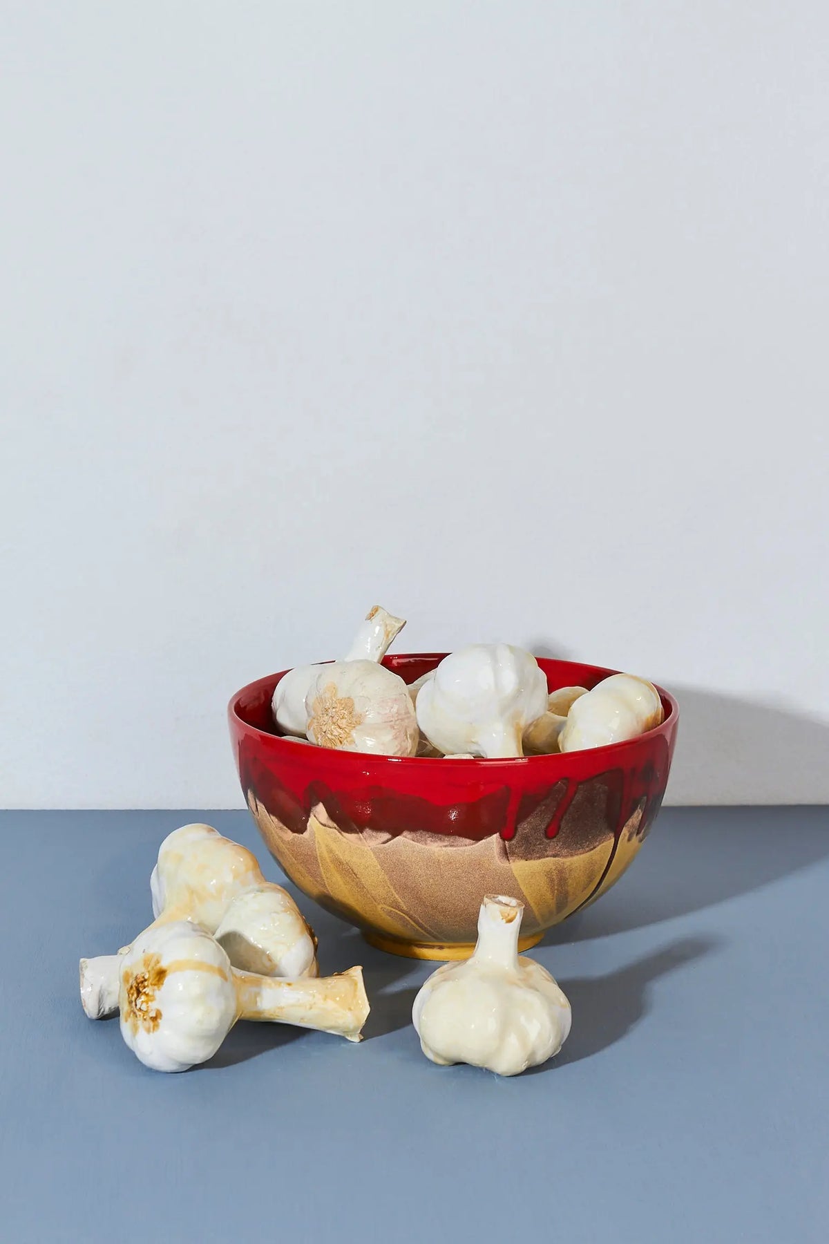Tazón rojo y dorado de cerámica con ajos decorativos en su interior. Ideal para cocina moderna.