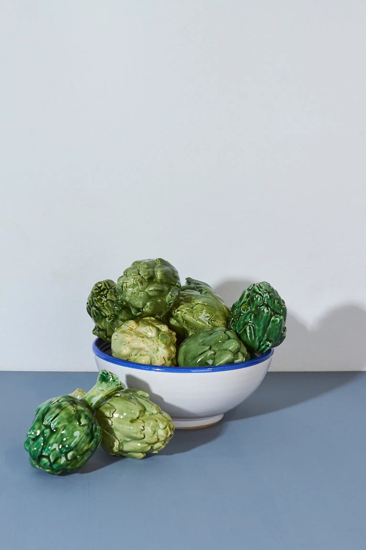 Tazón blanco con borde azul lleno de alcachofas verdes brillantes, decoración rústica y vibrante.