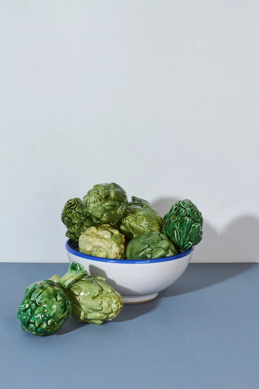 Tazón blanco con borde azul lleno de alcachofas verdes brillantes, decoración rústica y vibrante.