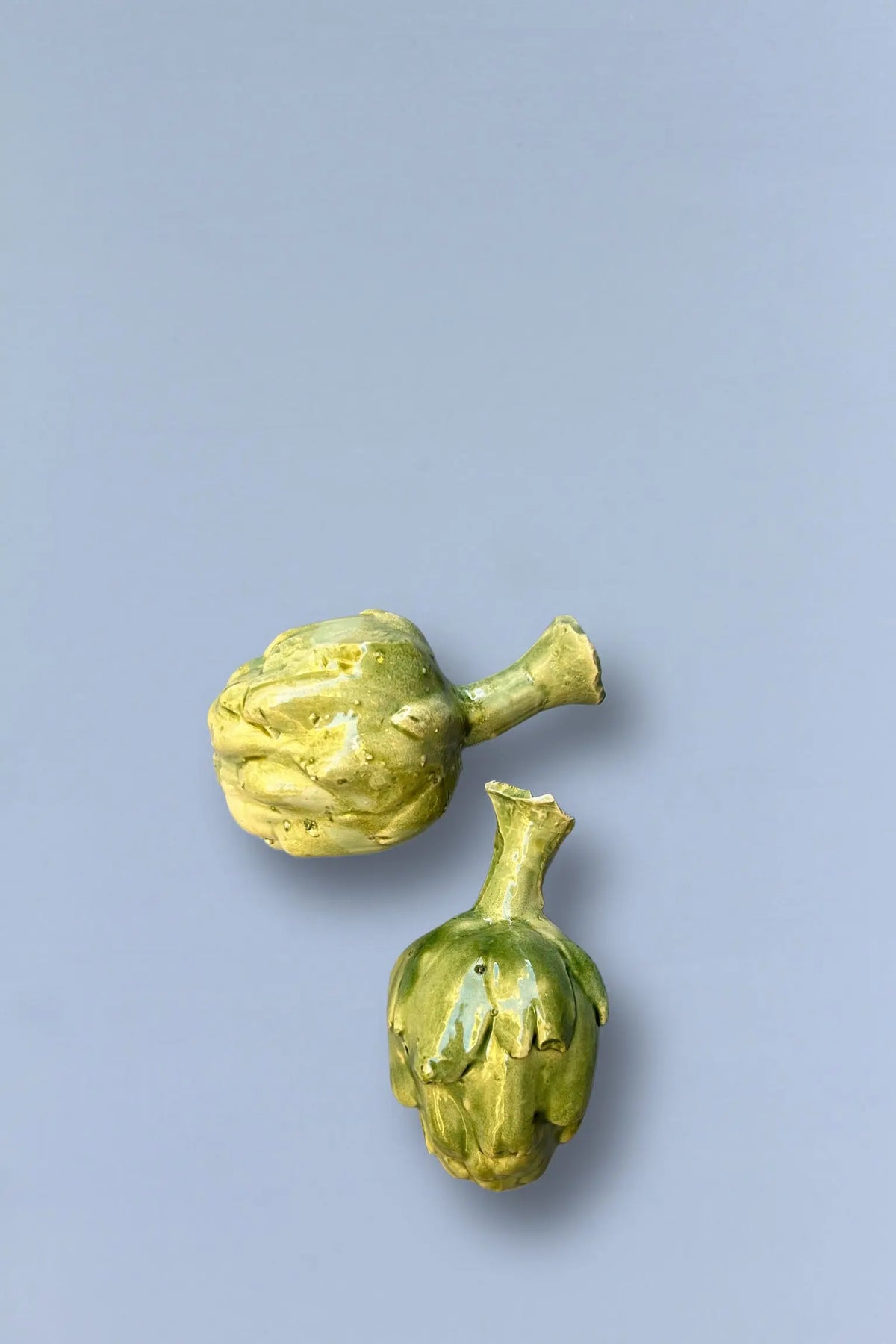 Dos alcachofas de cerámica en tonos verdes sobre fondo gris claro, ideales para decoración de cocina.