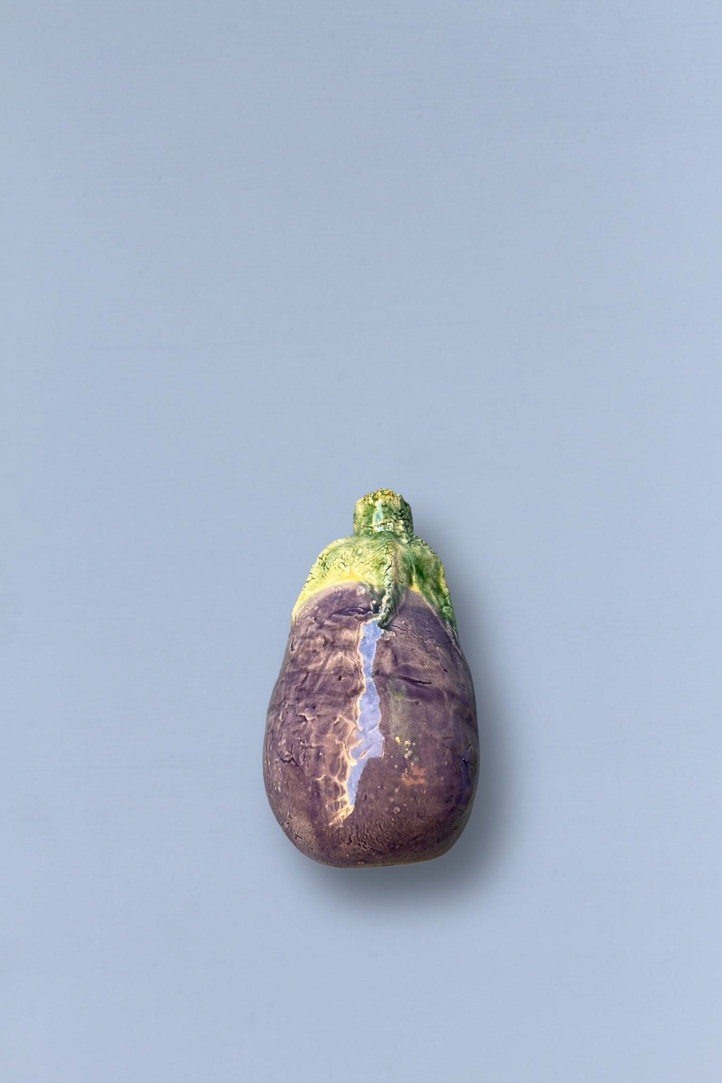 Figura de berenjena de cerámica brillante, en tonos morado y verde, ideal para decoración moderna o artística.