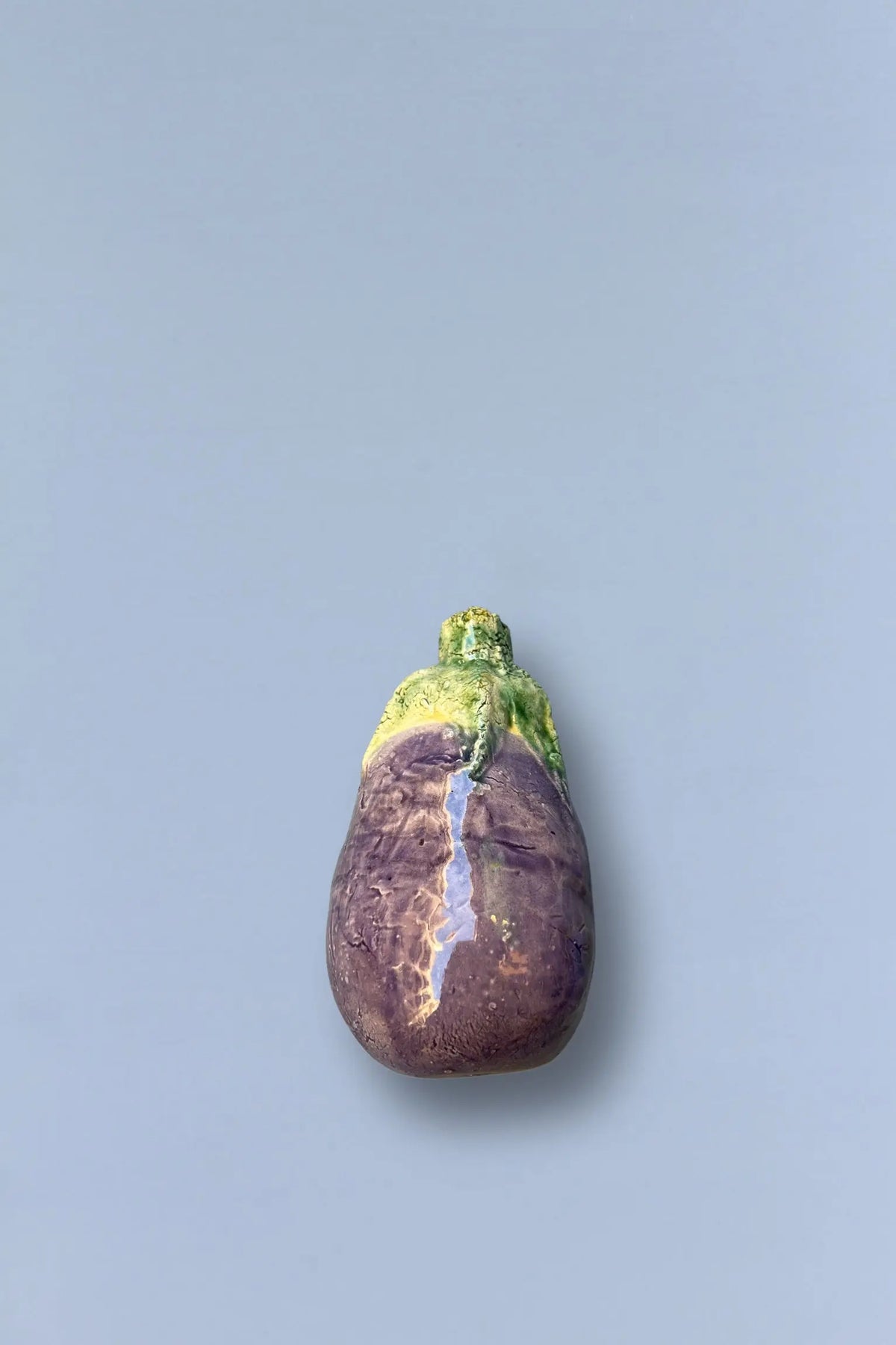 Figura de berenjena de cerámica brillante, en tonos morado y verde, ideal para decoración moderna o artística.