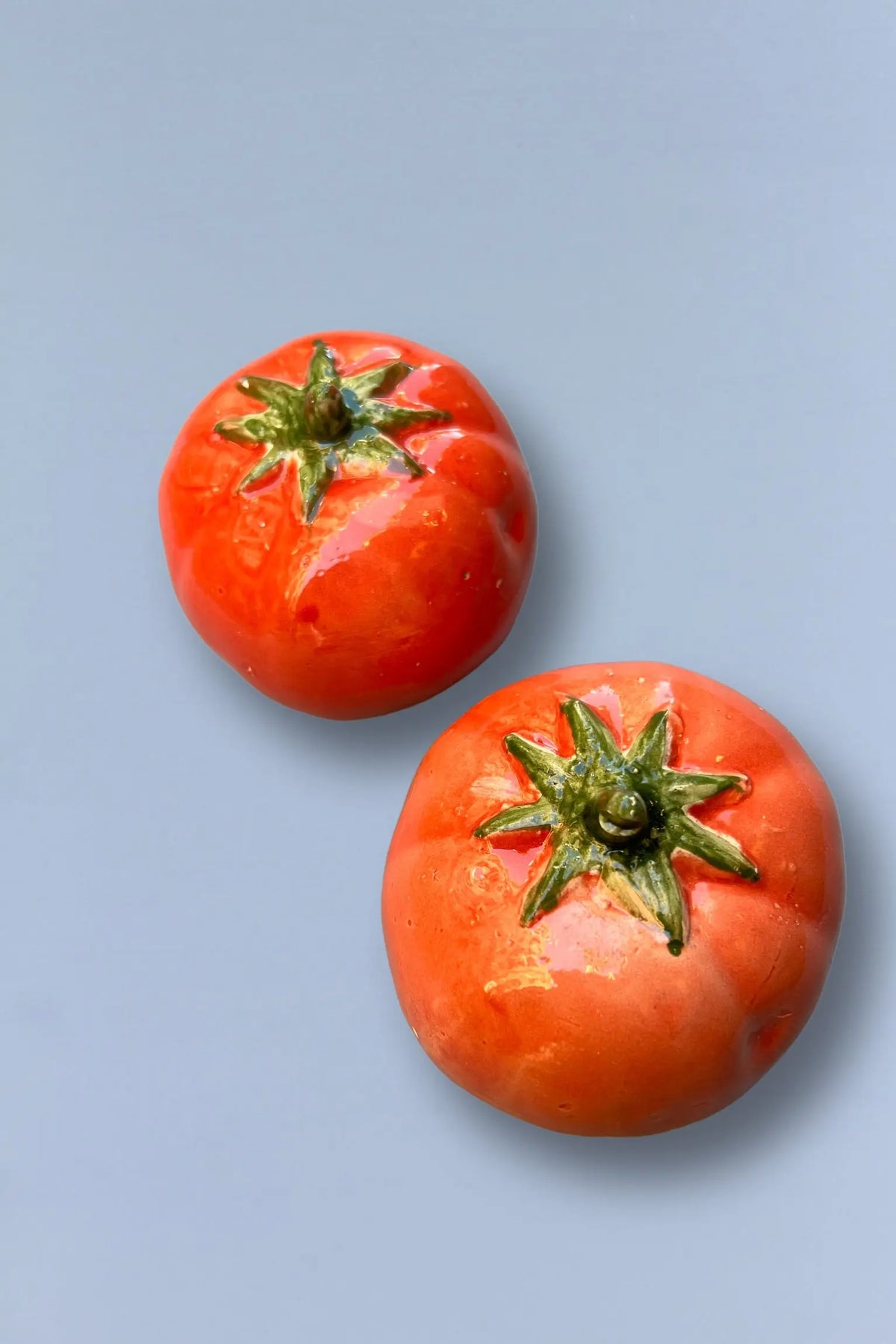 Tomates de cerámica roja brillante, decorativos, con detalles verdes, ideales para adornar mesas o cocinas.