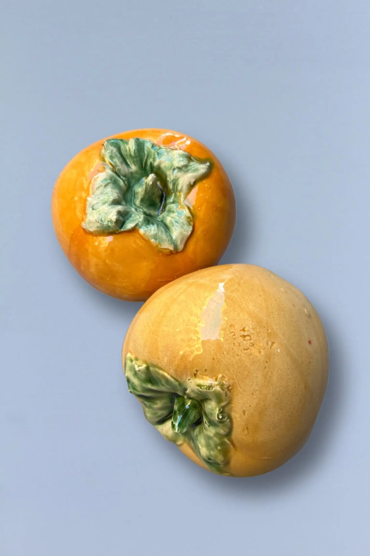 Jarrón de cerámica en forma de caqui, color naranja y verde, estilo moderno y decorativo.
