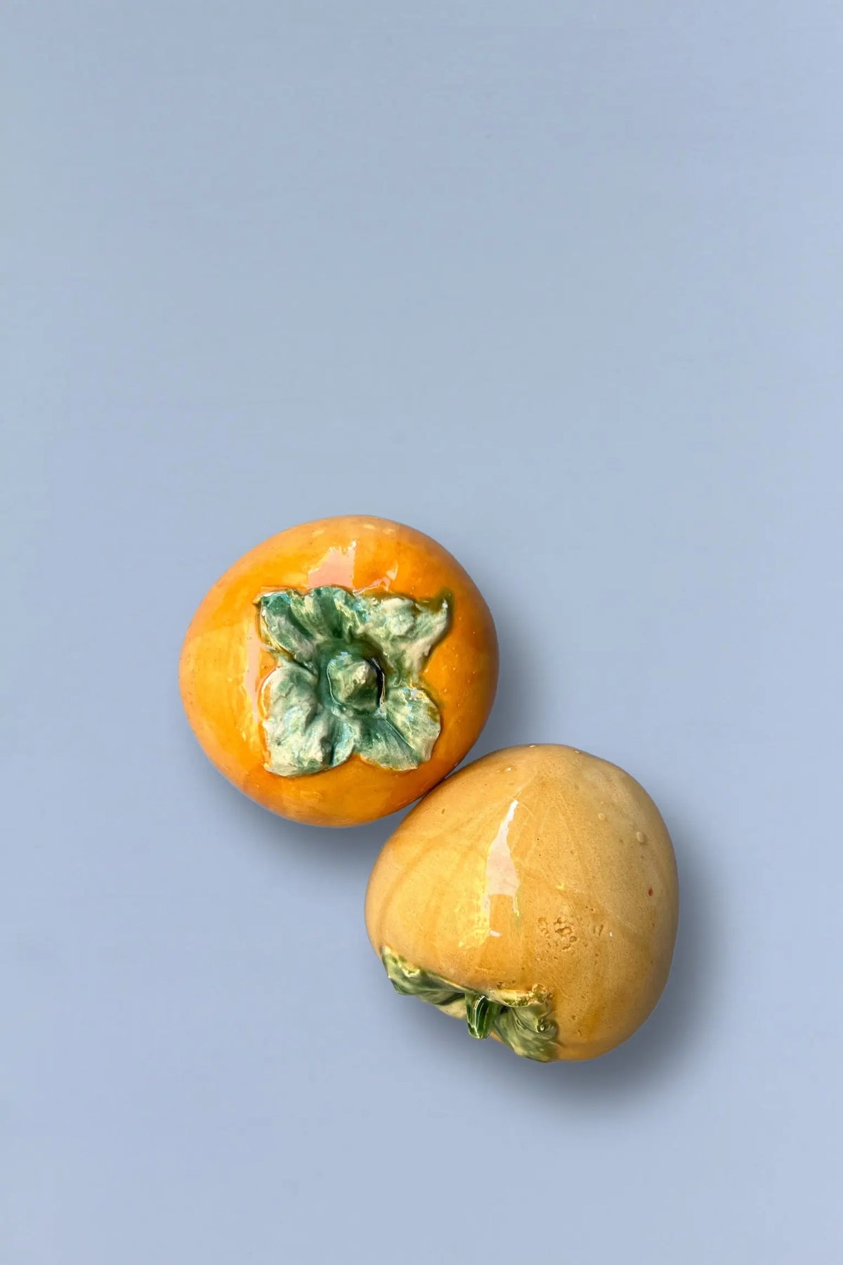 Frutas persimonas amarillas con hojas verdes en fondo azul claro, decorativas y realistas.