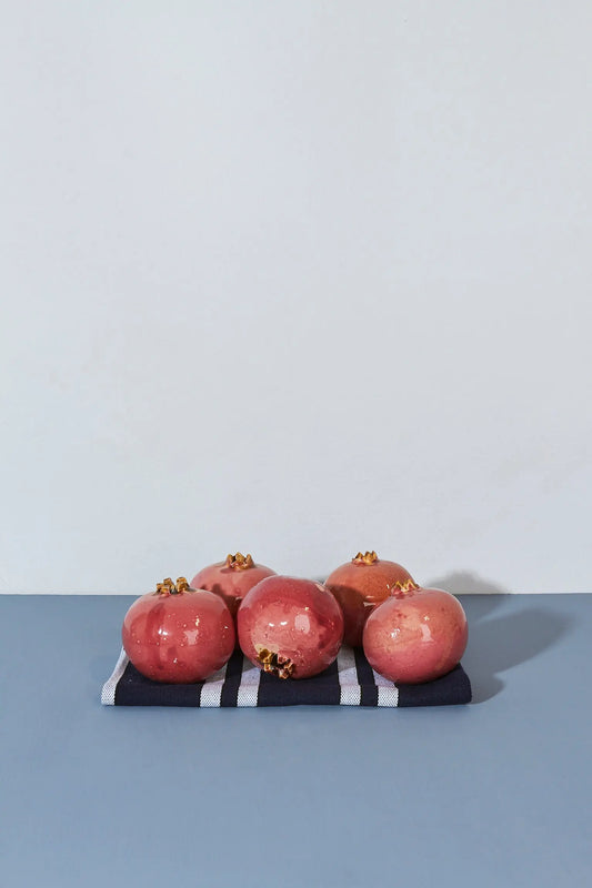 Granadas rosadas sobre una servilleta de rayas azules y blancas, con un fondo minimalista.