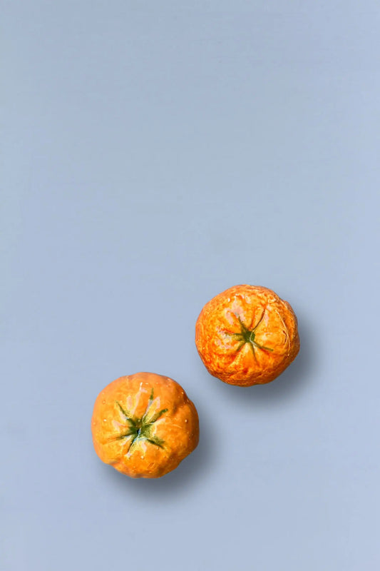 Dos mandarina pequeñas, color naranja brillante con textura rugosa, sobre un fondo azul suave.