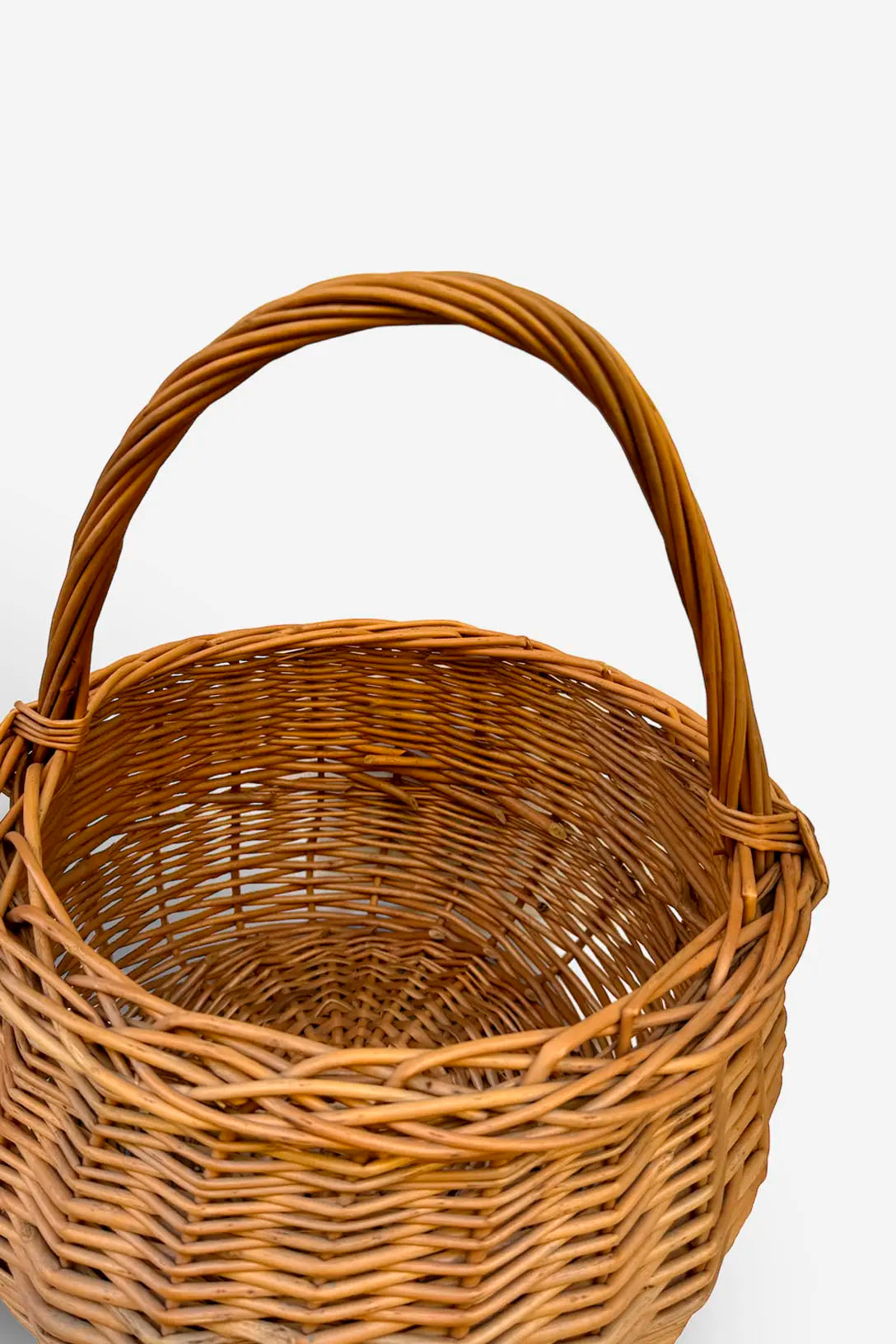 Cesta redonda de mimbre natural con trenzado artesanal y asa arqueada, en tono marrón claro. Fondo blanco.