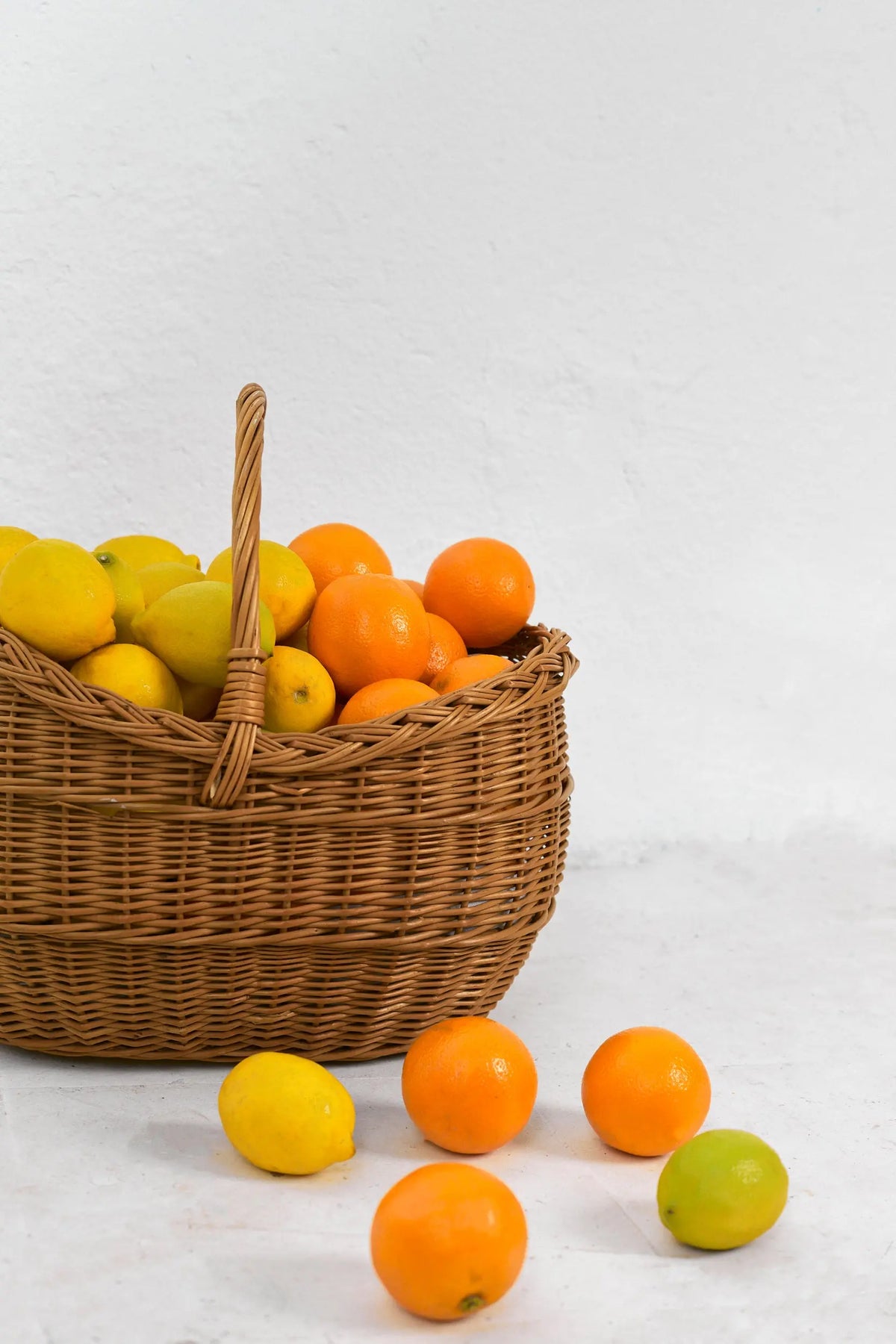 Natural wicker basket filled with fresh yellow lemons and bright orange oranges, on a white textured background.