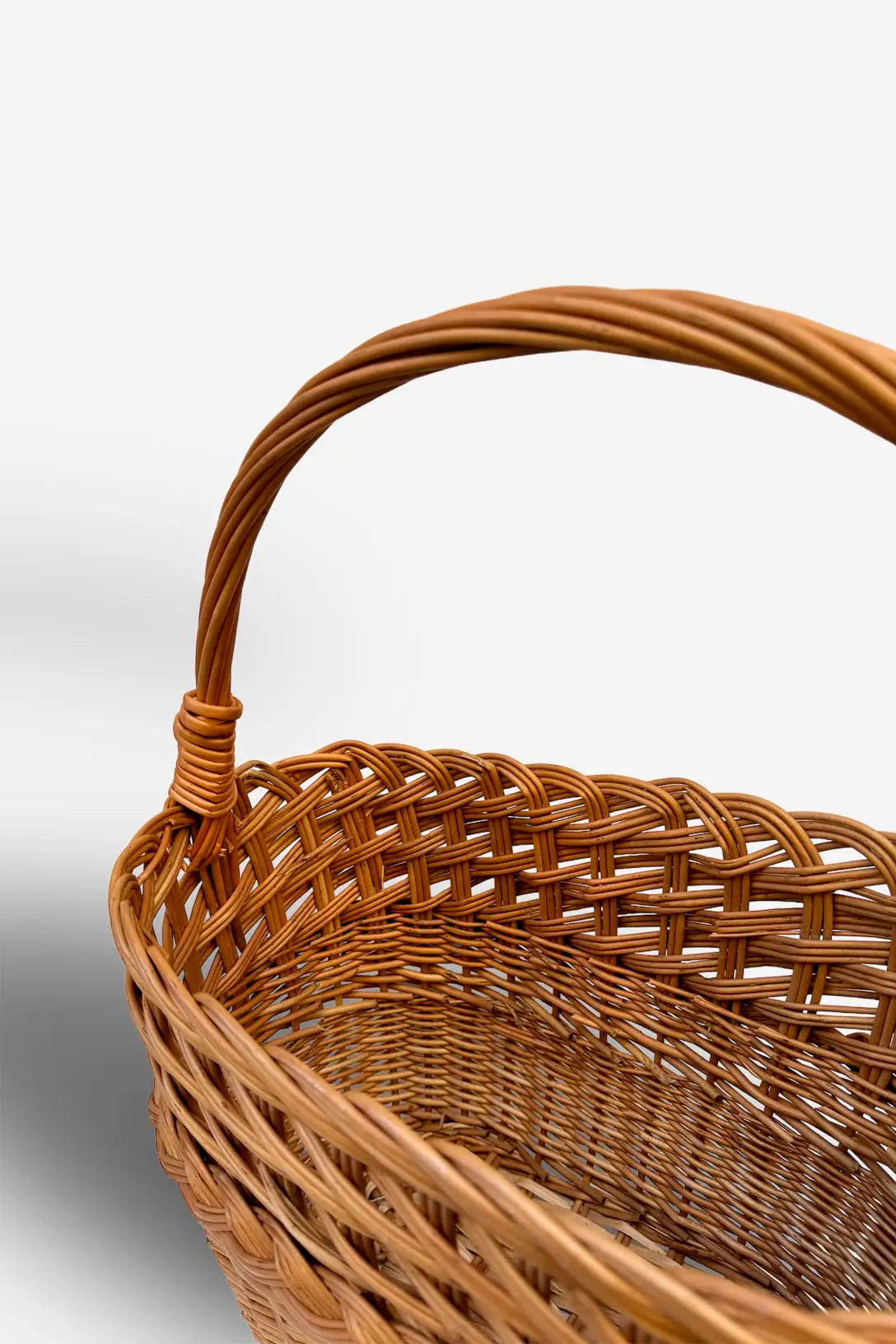 Cesta revistero de mimbre natural con trenzado artesanal y asa semicircular sobre un fondo blanco neutro.