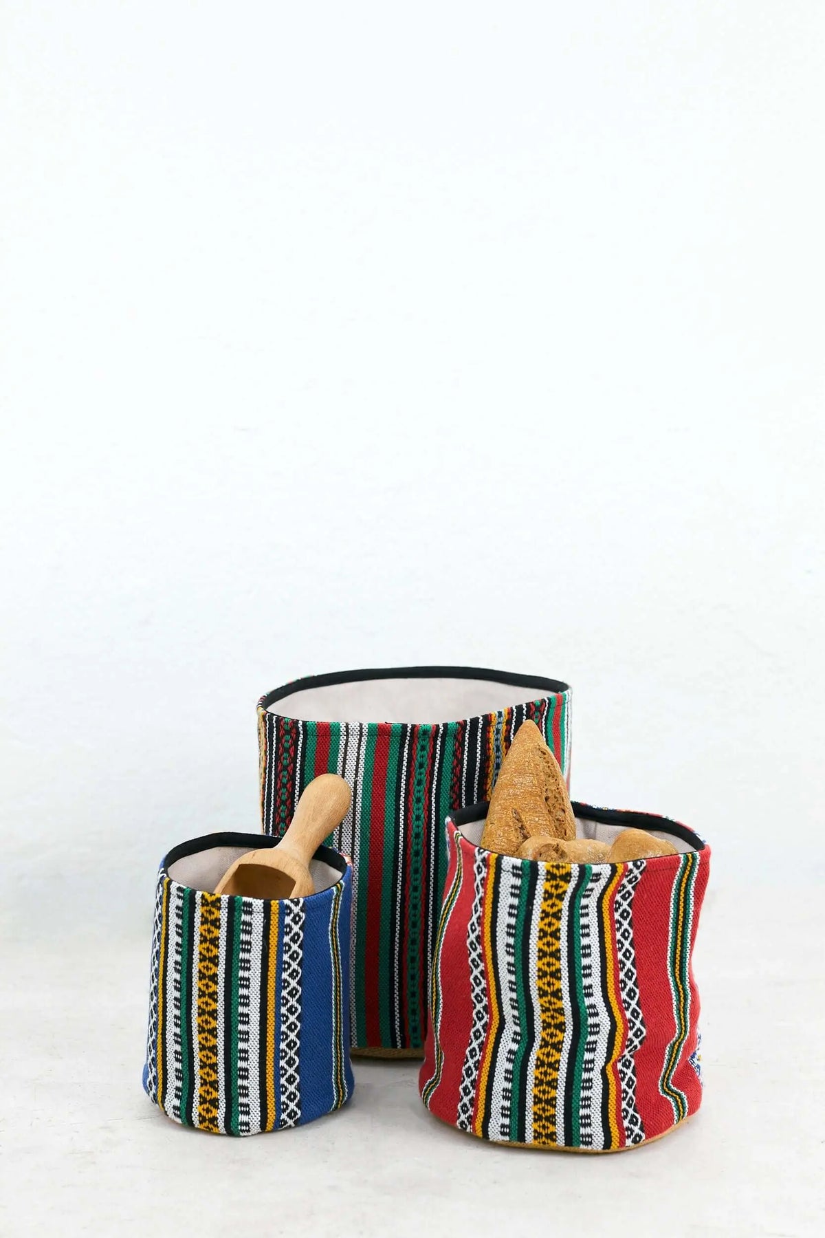 Tres cestos cilíndricos de tela con rayas verticales de colores vivos, patrones geométricos y un interior claro.