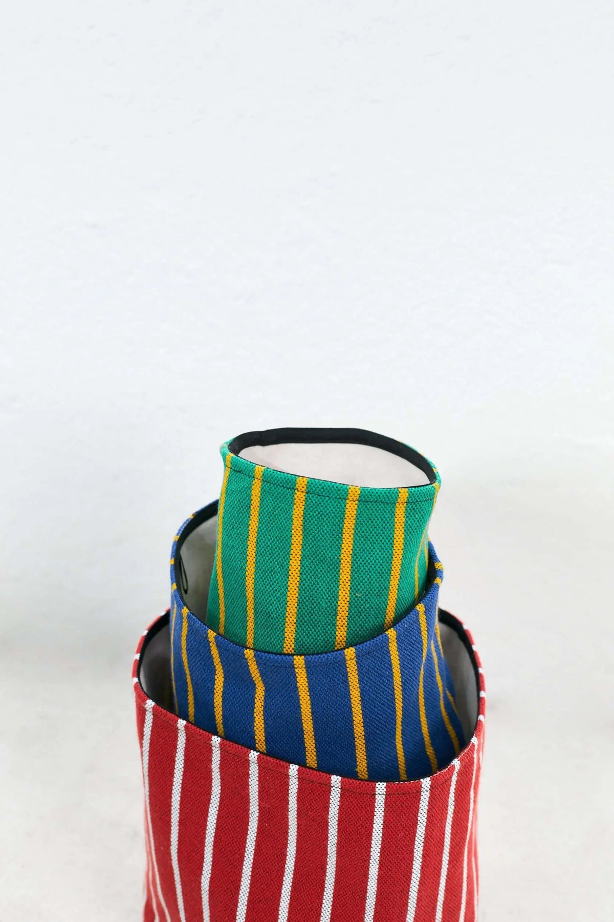 Set de tres cestos de algodón apilados con diseño a rayas en colores rojo, azul y verde sobre fondo blanco.