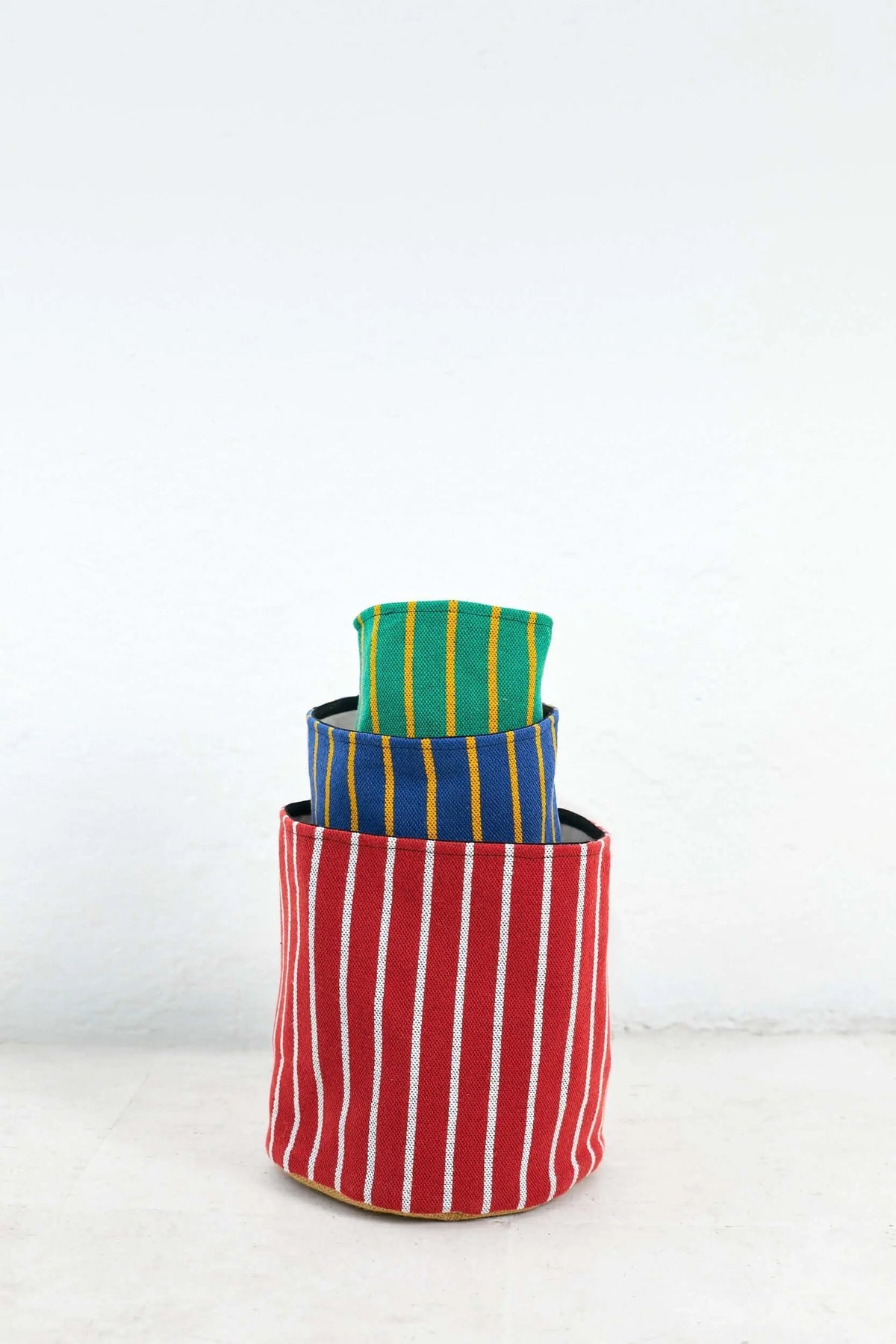 Set de tres cestos de algodón apilados con diseño de rayas coloridas: rojo, azul y verde sobre fondo blanco.