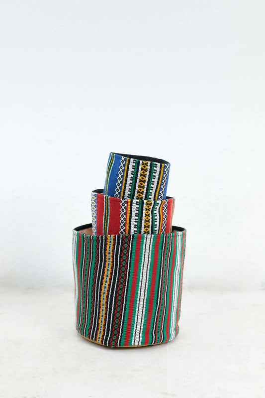 Tres cestos cilíndricos de tela con patrones geométricos y rayas verticales de colores intensos, apilados uno dentro otro.