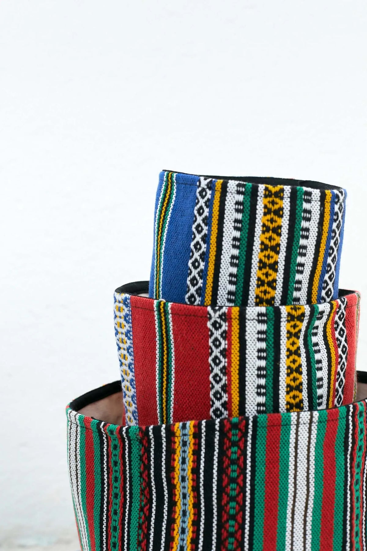 Tres cestos textiles apilados con estampados de rayas verticales de colores vivos y motivos geométricos tradicionales.