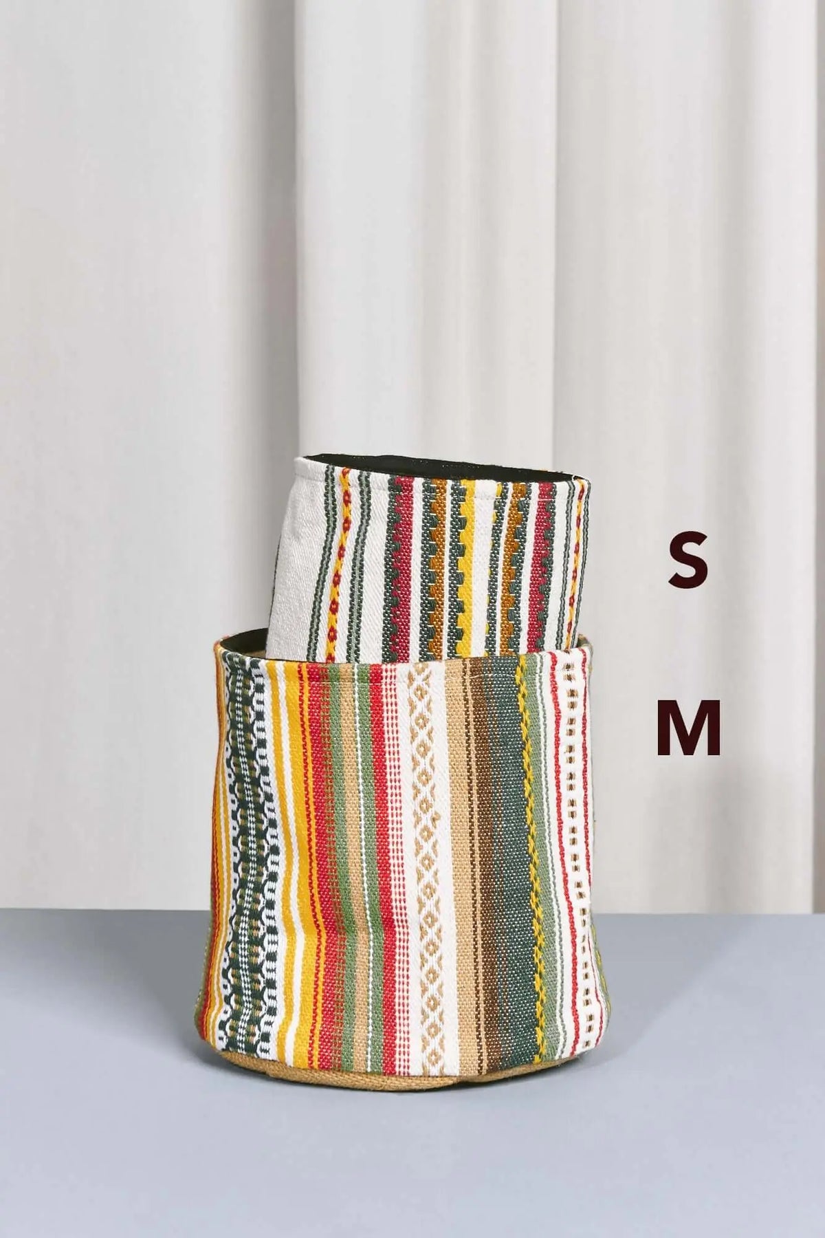 Dos cestos cilíndricos de tela con rayas verticales en tonos vivos como amarillo, rojo, verde y blanco. Tamaño S y M.