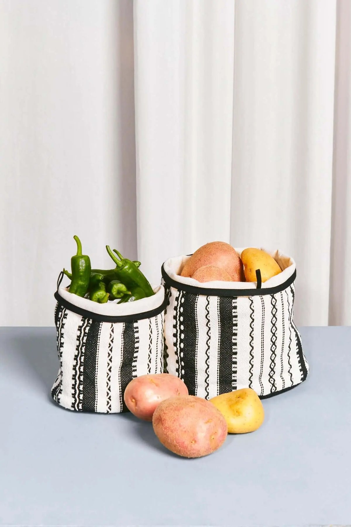 Two cylindrical fabric storage baskets with black and white striped geometric patterns filled with vegetables.