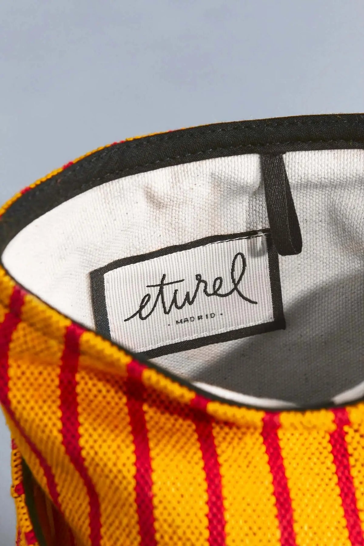 Red and yellow striped canvas storage basket with a black rim and white interior lining featuring an eturel label.
