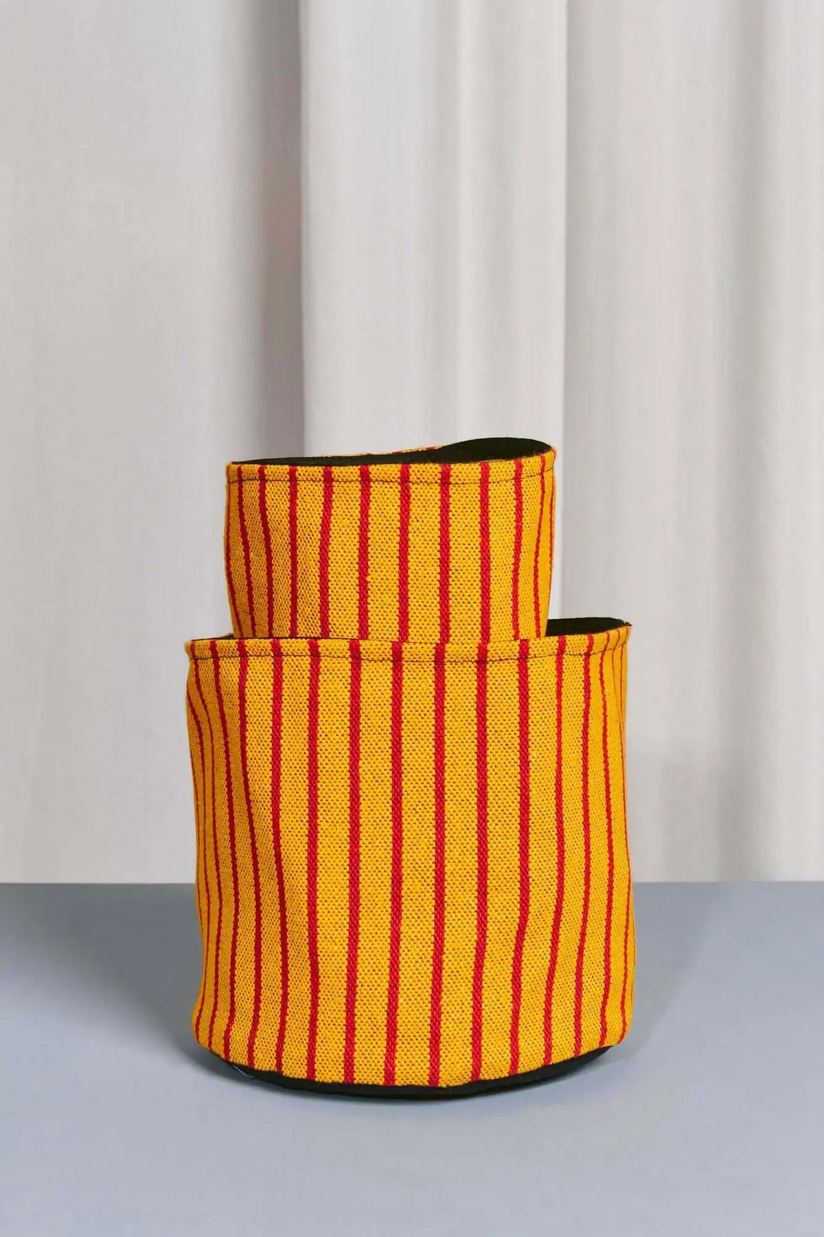 Yellow and red vertical-striped canvas fabric storage basket with a cylindrical shape and black interior lining.