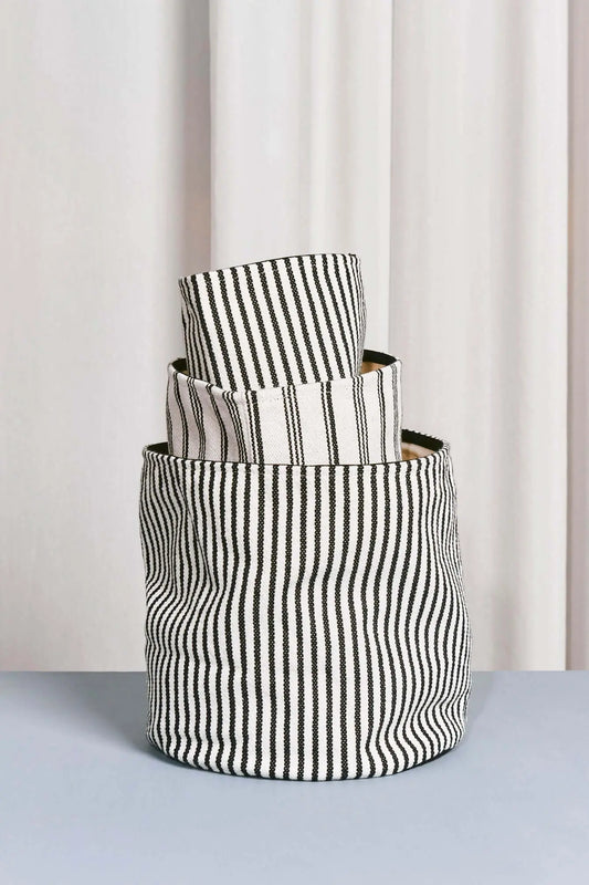 Conjunto de tres cestos de loneta cilíndricos con estampado de rayas verticales en blanco y negro.