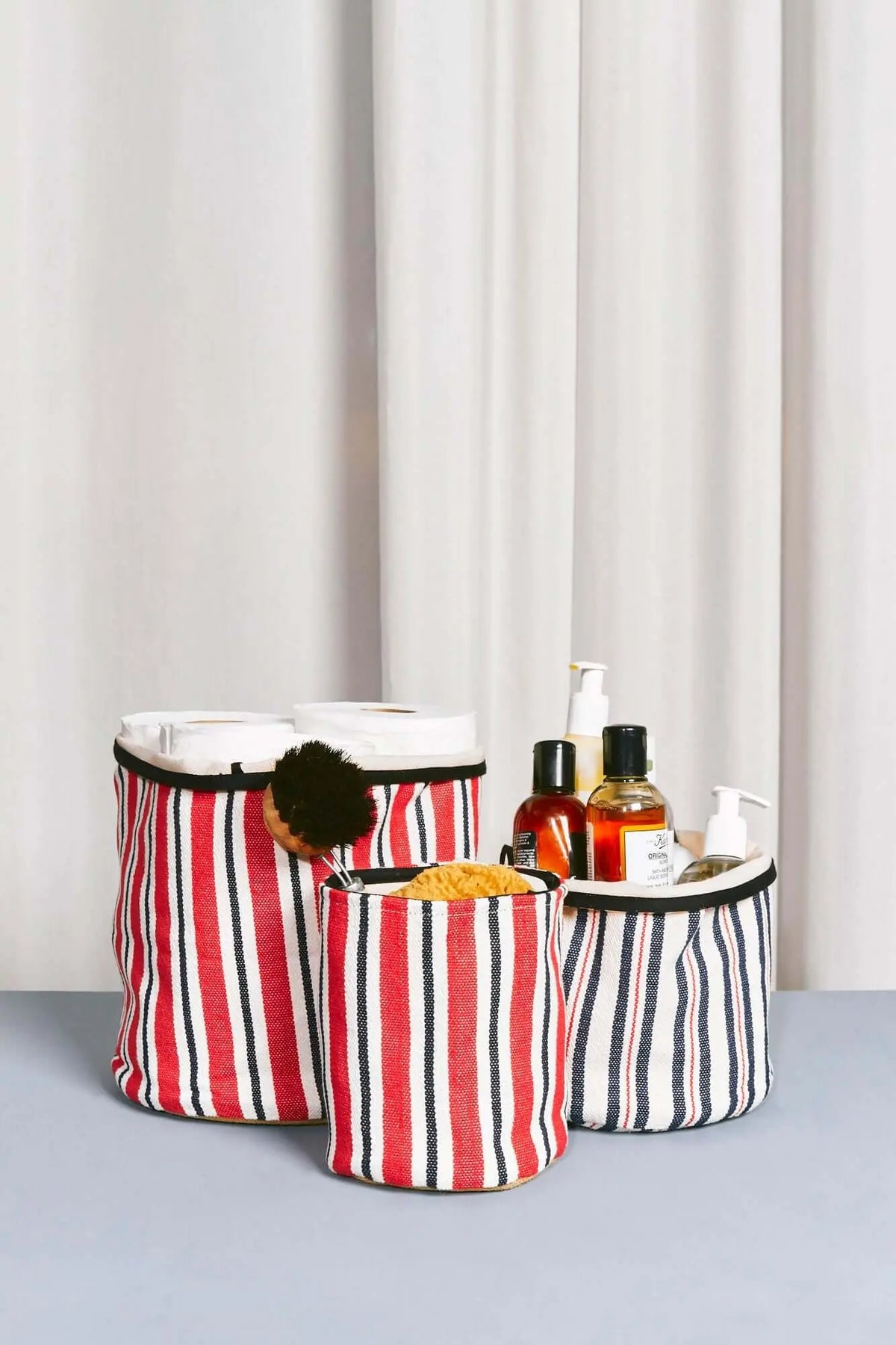 Cestos de loneta cilíndricos con rayas rojas, azules y blancas, ideales para organizar artículos de aseo y baño.